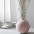 Pink vase with dried branches on a white surface with a light gray curtain background
