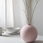 Pink vase with dried branches on a white surface with a light gray curtain background
