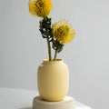 Yellow vase with yellow flowers on a white surface and light gray background