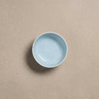 A small light blue speckled ceramic bowl centered on a textured beige background.