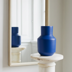 Blue vase on a white pedestal in front of a mirror reflecting another blue vase.
