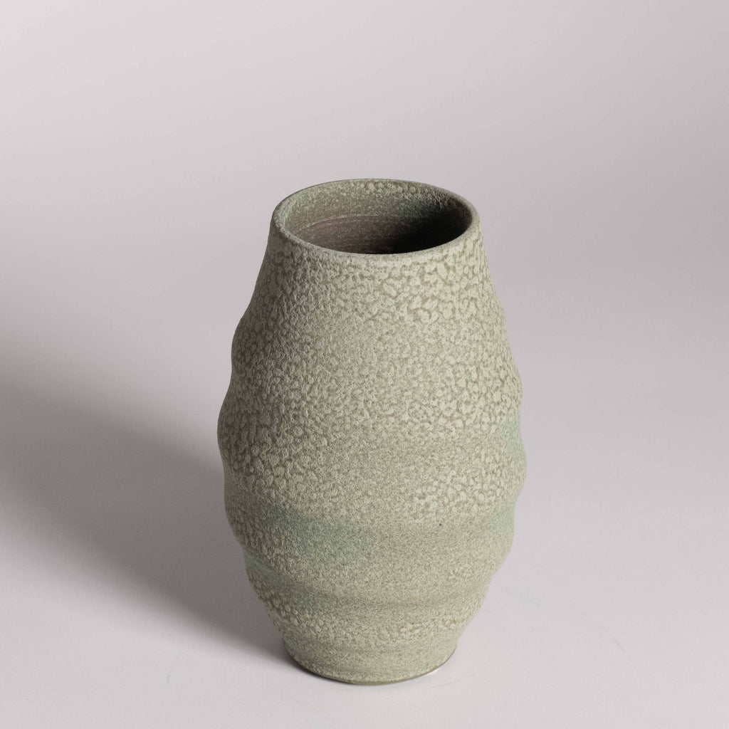 Textured green ceramic vase on a light gray background